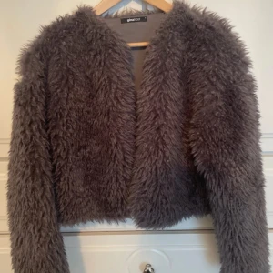 Mörkgrå pälsjacka från Gina Tricot - Säljer en fluffig och trendig mörkgrå pälsjacka från Gina tricot. Jackan har lång ärm och är perfekt för att ge en cool look till din outfit. Den är mjuk och har en klassisk rak passform.