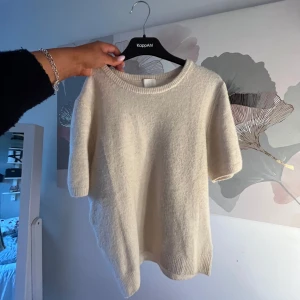 Beige stickad kortärmad tröja från H&M - Säljer en beige stickad tröja från H&M med korta ärmar och rund halsringning. Tröjan har en enkel och stilren design, perfekt för lager-på-lager eller sommarens svalare dagar.