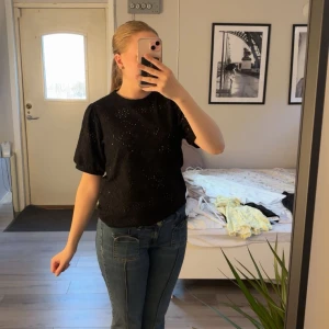 Svart blus från vero moda  - Superfin svart blus i lätt och luftig bomull med vackra broderade hålmönster. Perfekt både till vardags och fest! Kort ärm och rund halsringning. Blusen är även i stolek medium och används fåtal gånger❤️.
