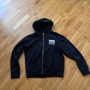 Svart hoodie med döskalletryck från Jack & Jones - Svart hoodie från Jack & Jones med dragkedja och huva. Perfekt för dig som gillar streetwear. Använd: Lite solblekt men inget farligt! Storlek S men den passar mig och jag är 180cm