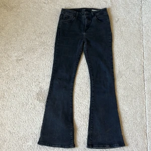 Svarta bootcut, mid waist jeans från Lois - Säljer ett par svarta bootcut jeans från Lois med klassisk femficksdesign och logga på bakfickan. Jeansen har normal passform och är tillverkade i ett mjukt denim tyg.
