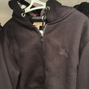 Svart hoodiejacka från Burberry - Säljare en fin Burberry-kofta i klassisk modell och snygg passform. Den är i storlek M, men upplevs något mindre i storleken – passar dig som vanligtvis har S eller en mindre M.  Koftan har använts och är i okej skick bara för 1100 pris kan diskuteras.