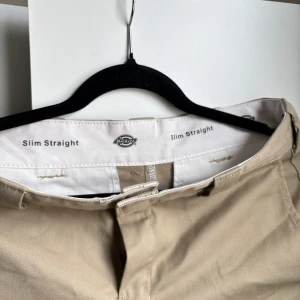 Beige Slim Straight byxor från Dickies - Säljer ett par klassiska beige byxor från Dickies i modellen Slim Straight. Byxorna har normal passform med raka ben och hällor för bälte. Perfekta till vardags för en clean och stilren look. Som en S!