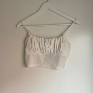 Vit croppad linnetopp - Säljer en vit croppad linnetopp med smala axelband och rynkade detaljer framtill. Perfekt för varma dagar och enkel att matcha med olika outfits.