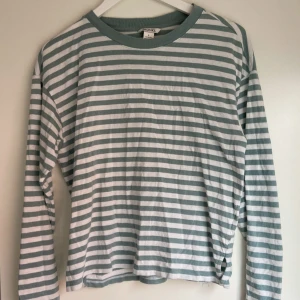 Randig långärmad tröja från Monki - Säljer en långärmad tröja från Monki med gröna och vita ränder. Tröjan har rund halsringning och är i mjuk bomull, perfekt för en avslappnad stil.