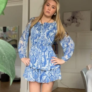 Blåvit mönstrad klänning med volang - Supersöt blåvit klänning med paisleymönster, knyte fram och volangkjol. Aldig använd med lappen kvar från Amisu💖