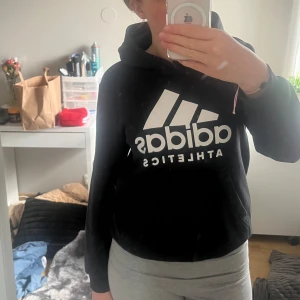 Svart hoodie från Adidas - Säljer en svart hoodie från Adidas med stor vit logga framtill. Tröjan har huva och långa ärmar med ribbade muddar. Perfekt för en sportig och avslappnad stil. Storlekslappen är avklippt men  är för liten på mig som är 162cm. Skulle säga den sitter som en xxs. Hör av er vid fler frågor eller bilder!💛