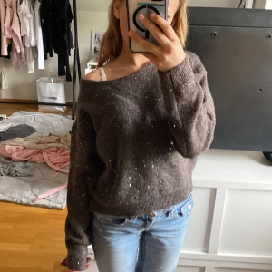 Brun glittrig stickad tröja från Gina Tricot - Säljer en brun stickad tröja från Gina Tricot med glittriga paljettdetaljer. Tröjan har en lös passform och kan bäras off-shoulder. Perfekt för dig som vill ha något extra till vardagslooken.