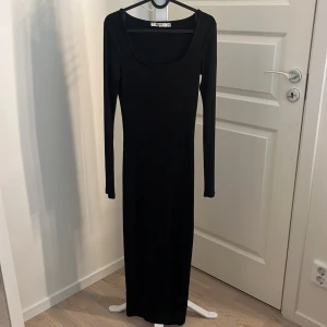 Svart långklänning från NA-KD - Säljer en svart långklänning från NA-KD med rund halsringning och långa ärmar. Klänningen är ribbad och har en slits framtill för extra rörelsefrihet. Perfekt för dig som gillar en stilren och enkel look.🌺