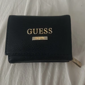 Blå plånbok från Guess🌼 - Säljer en stilren mörkblå plånbok från Guess med guldfärgade detaljer och logga framtill. Plånboken har dragkedja runt kanten och tryckknapp på insidan. Perfekt storlek för kort och kontanter. Använd gärna köp nu!💗🌸