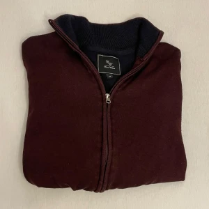 Vinröd kofta med fullzip  - Mörkröd kofta med hel dragkedja. Har lång ärm, ribbad krage och muddar. Perfekt lager-på-lager och enkel att matcha med olika outfits.