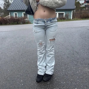 Ljusblå slitna bootcut jeans - Ljusblå jeans med slitningar och hål på framsidan av benen. Byxorna har bootcut-stil och är lågmidjade. Klassisk femficksmodell med dragkedja och knapp framtill. Pris kan dirkuteras vid snabb affär. Midjemått: 37 innerbenslängden: 82