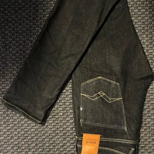 Replay Anbass Hyperflex jeans i svart denim - Säljer ett par svarta Replay Anbass Hyperflex jeans med slim fit. Jeansen har klassisk femficksdesign, snygga kontrastsömmar och läderpatch bak i midjan. Perfekta för dig som vill ha stretchiga och bekväma jeans med stilren look.
