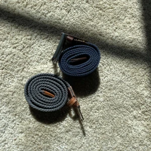 Två flätade herrbälten i blått och grått - Säljer två stilrena flätade bälten, ett i mörkblått och ett i grått. Båda har detaljer i brunt läder och metallspänne. Perfekta för att lyfta din outfit med en modern touch. Den mer blåa bältet har en stor effekt vid spännet be om närmare bilder om du är intresserad!