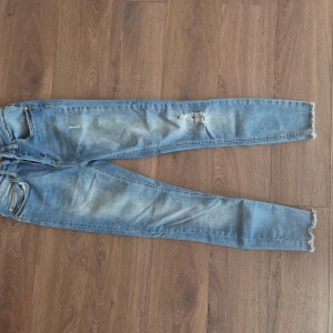 Blå skinny jeans från ONLY med slitningar - Säljer ett par ljusblå skinny jeans från ONLY med slitningar vid knät och råa benslut. Klassisk femficksmodell med dragkedja och knapp. Perfekta för en avslappnad och trendig look. Aldrif använd