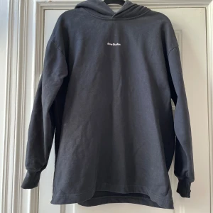 Svart hoodie från Acne Studios - Säljer en svart hoodie från Acne Studios med logga på bröstet. Tröjan har långa ärmar, huva och är tillverkad i mjuk bomull. Perfekt för en avslappnad och stilren look.