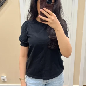 Svart t-shirt med puffärm - Svart t-shirt med rund halsringning och korta puffärmar. Enkel och stilren modell som passar till mycket. Tillverkad i mjukt material och har en normal passform.