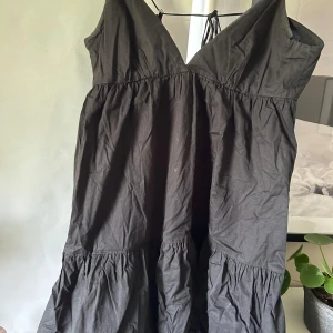Svart klänning med volang och v-ringning - Säljer en svart klänning med v-ringad hals och volangdetaljer. Klänningen har smala axelband och en luftig passform, perfekt till sommaren