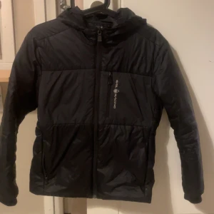 Svart pufferjacka från Sail racing  - Svart pufferjacka från sailracing med huva och dragkedja framtill. Jackan har en bröstficka med dragkedja och logga på vänster sida. Perfekt för kyligare dagar och enkel att matcha med olika outfits. Skriv för funderingar eller frågor 💯💯💯