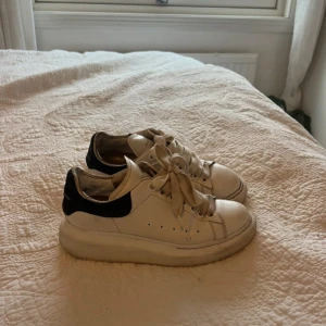 Vita sneakers från Alexander McQueen - Säljer ett par klassiska vita sneakers från Alexander McQueen med svart hälparti och tjock vit sula. Skorna har snörning och en stilren design som passar till många outfits. Jätteslitna. Har fler bilder om det behövs