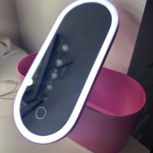 Rosa sminkspegel med LED-belysning och förvaringsbox - Snygg rosa helt ny sminkspegel med inbyggd LED-belysning och touchknapp. Ljuser går att justeras. Spegeln är avtagbar men är perfekt att sätta på rosa förvaringslådan, perfekt för sminkborstar och andra sminkaccessoarer. Praktiskt handtag för enkel transport. Kommer i orginalförpackning och kabel medförs, går även att använda batterier.
