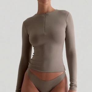 Beige långärmad topp med dragkedja - Snygg beige långärmad topp med tight passform och diskret dragkedja framtill vid halsen. Tillverkad i ett mjukt och stretchigt material som sitter skönt mot kroppen. Perfekt att styla till både jeans och kjol.