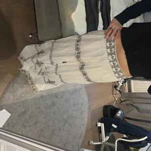Vit långkjol med broderade detaljer - Säljer en vit långkjol med svarta broderade mönster och dekorativa band. Skriv om du har några frågor 💕
