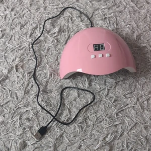 Rosa UV-lampa för naglar med digital display - Säljer en rosa UV-lampa för naglar med digital display och tre vita knappar (30, 60, 90 sek). Lampan har flera LED-lampor på insidan och ansluts via USB. Perfekt för att härda gel- eller shellacklack hemma.