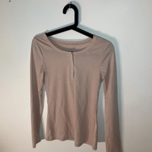 Beige ribbad långärmad topp från SHEIN - Säljer en beige ribbad långärmad topp från SHEIN i storlek S. Toppen har rund halsringning och knappar framtill. Tillverkad i mjukt och stretchigt material med 95% polyester och 5% elastan.
