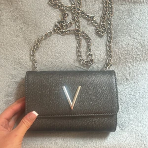 Grå valentino väska - Grå valentino väska med V detalj. V-et har börjat rosta lite men det syns mer på bild än i verkligheten. 