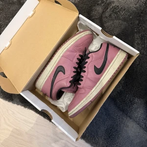 Nike Air Jordan 1 Low SE i lila och svart - Säljer ett par Nike Air Jordan 1 Low SE i en snygg lila färg med svarta detaljer och vit sula. Skorna har klassisk låg siluett, svart swoosh och svarta skosnören. Perfekta för dig som vill sticka ut med dina sneakers. Använt skick 
