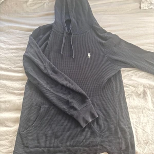 Mörkblå hoodie från Ralph Lauren - Säljer en stilren mörkblå hoodie från Ralph Lauren med en liten broderad logga på bröstet. Tröjan har långa ärmar och en klassisk huva. Perfekt för en avslappnad look. En liten defekt 