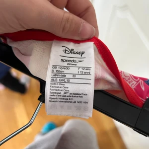 Disney x Speedo färgglad bikini - Färgglad bikini från Disney x Speedo med mönster av Mickey Mouse i blått, gult och rött. Toppen har smala röda axelband och matchande kant, och bikinitrosan har samma färgglada print. Perfekt för dig som vill sticka ut på stranden!