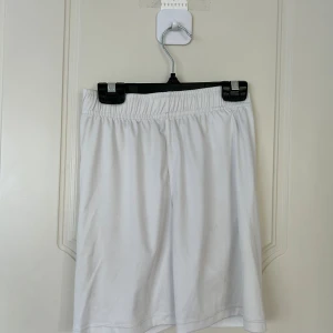 Vita träningsshorts från SOC - Vita shorts från SOC med elastisk midja och enkel, clean design. Perfekta för träning eller sport, tillverkade i lätt polyester som andas. Passformen är normal och materialet känns mjukt mot huden. Snygga att matcha med en t-shirt eller hoodie.