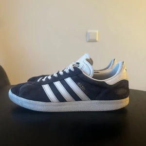 Adidas Gazelle i mörkblå mocka 42 2/3 - Säljer ett par klassiska Adidas Gazelle sneakers i mörkblå mocka. Storlek 42:2/3. Blåa skosnören medföljer vid köp 🙃