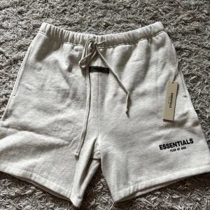 Essentials Fear of God shorts ljusgrå - Snriv för fler bilder! HELT NYA!Snygga ljusgrå shorts från Essentials Fear of God med elastisk midja och snörning. Mjukt bomullsmaterial och stilren logga tryckt på benet. Perfekta för chill dagar eller när du vill ha en clean streetwear-look.