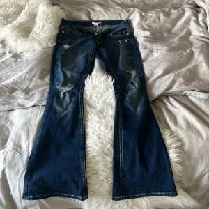 Bootcut jeans från Gina Tricot S - Snygga mörkblå bootcut jeans från Gina Tricot med slitna detaljer och broderade bakfickor. Jeansen har kontrastsömmar, klassisk femficksdesign och dragkedja med knapp. Perfekt för dig som gillar retrovibbar och vill sticka ut med coola detaljer.