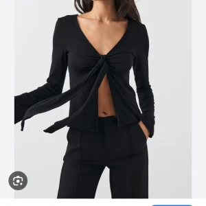 Svart omlottopp med knyt från Gina Tricot - Svart långärmad omlottopp från Gina Tricot i storlek M. Toppen har en djup v-ringning och cool knytning framtill som ger en croppad look. Materialet är mjukt och stretchigt, perfekt för att skapa en trendig outfit. Snyggt flow i ärmarna och stilren design. Ganska knopprig 