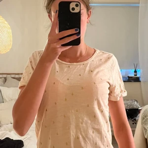 Ljusrosa t-shirt med prickigt mönster - Söt ljusrosa t-shirt från SEN med små prickar i ett diskret mönster över hela plagget. T-shirten har rund hals, korta ärmar med uppvik och är gjord i mjuk bomull. Perfekt för dig som gillar en chill och enkel stil.