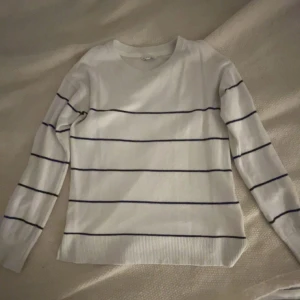 Vit randig långärmad tröja - Vit långärmad tröja med tunna svarta horisontella ränder. Tröjan har rund halsringning och ribbade muddar vid ärmslut och nederkant. Perfekt för en clean och avslappnad stil.