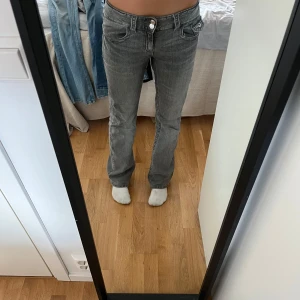 Grå bootcut jeans med låg midja - Säljer ett par grå jeans med bootcut och låg midja. Jeansen har klassisk femficksdesign, dragkedja och knapp framtill. Snyggt slitna detaljer och raka ben som blir vidare nertill. 