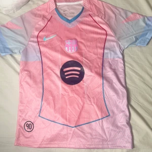 Barça x Nike rosa fotbollströja M - Säljer en limited edition FC Barcelona x Nike fotbollströja i rosa med ljusblå detaljer och vit-rosa mönster. Kortärmad med V-ringad krage i blått, tryckt Spotify-logga och klubbmärke på bröstet. Tillverkad i lätt, ventilerande Dri-FIT-material.