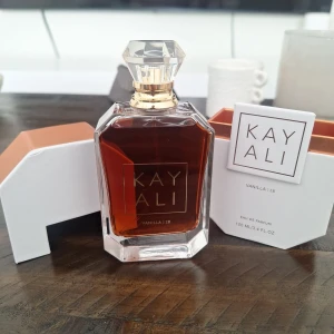 Kayali Vanilla | 28 Eau de Parfum 100ml - Kayali Vanilla | 28 är en lyxig parfym i en elegant, genomskinlig glasflaska med guldiga detaljer och kristalliknande kork. Doften har noter av vaniljorkidé, tonkaböna, brunt socker, amberträ och mysk. Flaskan rymmer 100 ml och kommer i en stilren vit och kopparfärgad ask.