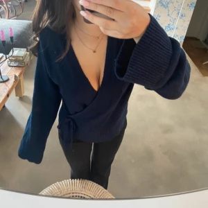 Mörkblå omlottkofta med knyt från Gina storlek 170 - Mysig mörkblå stickad omlottkofta med breda ärmslut och knyt i sidan. Djup v-ringning och långärmad modell, perfekt för lager-på-lager. Snygg och enkel att styla till både jeans och kjol.