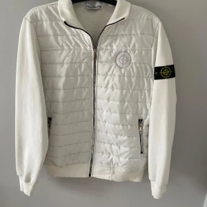 Stone Island cardigan/jacka - En skit Snygg vit cardigan/jacka från Stone Island med quiltad front och ärmar i mjuk bomull. Jackan har dragkedja, ribbade muddar och klassisk logga på ärmen. Perfekt för dig som gillar stilren klädsel, passar till allt och är extremt skön! Lite fläckar som du ser på sista bilden men som kanske går bort i en till tvätt, skicket är bra och i storlek M, hör av dig vid minsta fundering🤩
