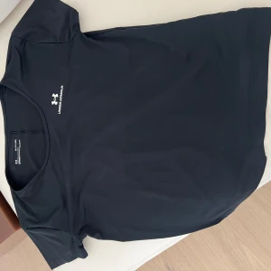 Svart träningst-shirt från Under Armour - Svart träningstshirt från Under Armour med rund hals och korta ärmar. Diskret logga och text på bröstet. Storlek xs men passar storlek S