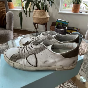 Vita och grå sneakers från Philippe Model - 4/10Sneakers i vitt skinn med grå mockadetaljer och bruna mockahälkappor från Philippe Model👟. Klassisk låg modell med snörning och platt sula. Snyggt slitna detaljer och diskret logga på sidan. Perfekta för en avslappnad streetstil🫶🏻😁. Den blåa fläck en svår att se när man väl bär skorna men det är det som sänker priset🙌 Priset är inte hugget i sten💸