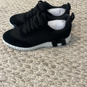 H3rmes skor - Svarta sneakers från H3rmes med vit, räfflad sula och coola svarta detaljer på yttersulan. Ovandelen är i mesh och mocka för en modern look. Skorna har snörning och en sportig, chunky vibe som sticker ut.