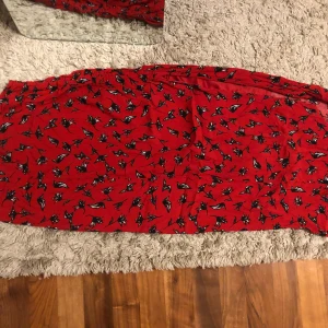Röd blommig kjol från Stradivarius - Röd kjol från Stradivarius med svartvitt blommönster. Kjolen har resår ner för ena låret och är tillverkad i ett mjukt, lätt material som känns skönt mot huden. Perfekt för dig som gillar färg och mönster och vill sticka ut lite extra. Kjolen går ner till vaden💗💗Den har en satin underkjol🫶🏻