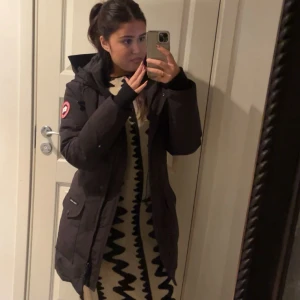 Stickad beige och svart klänning - Säljer en stickad långärmad klänning i beige med svarta, vågiga mönster längs hela plagget. Klänningen är figurnära och har rund halsringning. Perfekt för dig som gillar unika mönster och vill ha något som sticker ut.